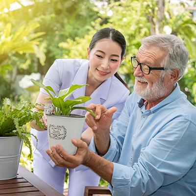 smiling resident and nurse outside in the garden and potting plants
